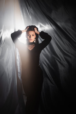 Pretty beautiful girl standing, posing, holding black curtains in her hands and playing with them. fashion studio portraitの写真素材