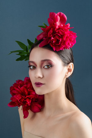 Beautiful young woman with long hair posing with peonies on her head. Portrait of a girl with flowers on her head.の写真素材