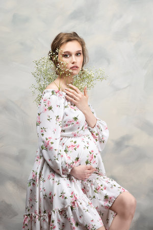 Beautiful pregnant woman with flowers on belly. Young woman in maternity waiting for baby birth. Pregnancy, Motherhood, Mother's Day Holiday concept.の写真素材