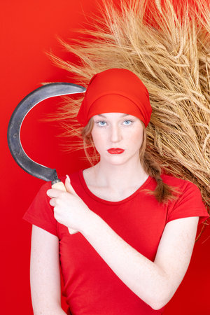 Female in red with a sickle in her hand on red backgroundの写真素材