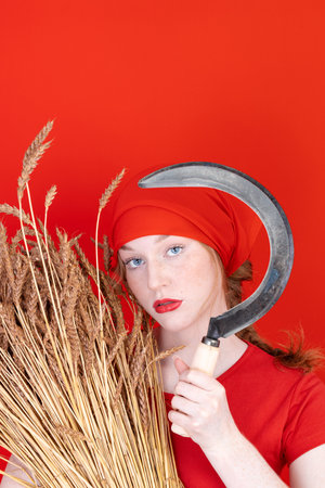 Female in red with a sickle in her hand on red backgroundの写真素材
