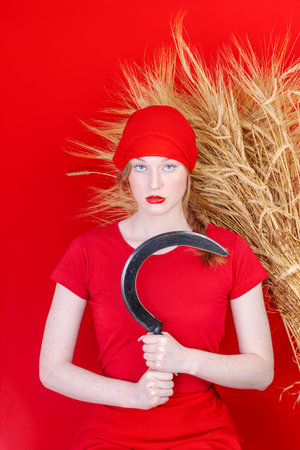 Female in red with a sickle in her hand on red backgroundの写真素材