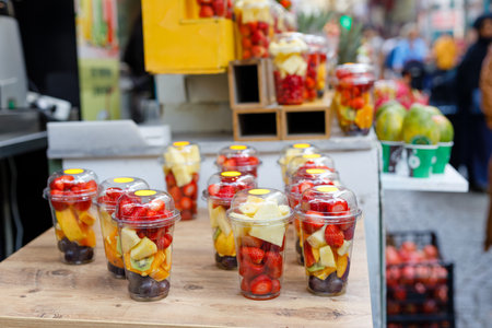 Fruit slices in transparent plastic cups with forks on a street market counter. Refreshing bright fruits on a hot summer sunny day.の写真素材