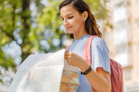 woman traveler holding location map in hands while looking for direction in urban scene in sunny summer dayの写真素材
