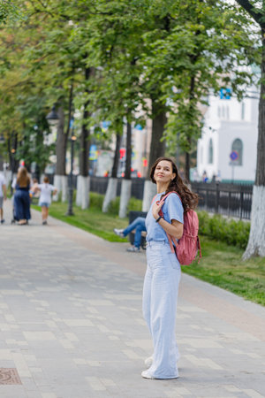 stylish positive middle aged female in jeans and sneakers strolling along city streetの写真素材