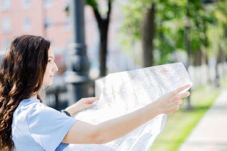 woman traveler holding location map in hands while looking for direction in urban scene in sunny summer dayの写真素材