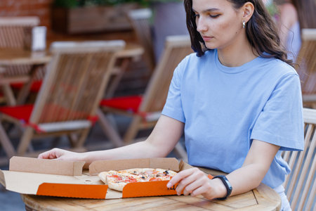 Attractive woman open pizza box and eating pizza outdoor cafeの写真素材