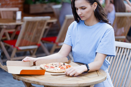 Attractive woman open pizza box and eating pizza outdoor cafeの写真素材