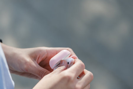 Close up of a woman hands taking off earbuds from case walking in the streetの写真素材