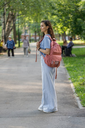 stylish positive middle aged female in jeans and sneakers strolling along city streetの写真素材