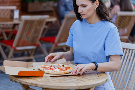 Attractive woman open pizza box and eating pizza outdoor cafeの写真素材