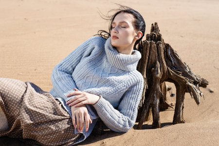 Young woman in warm clothes sitting on river bank alone on cool sunny day, enjoying peace and freedom side view. Outdoor weekend activityの写真素材