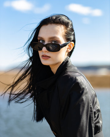 Caucasian young pretty stylish woman near river lake water street on sand pier dressed brown trench...