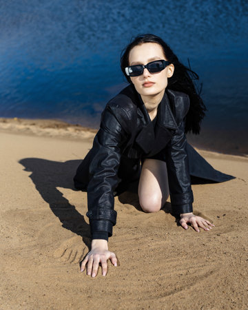Happy young woman in warm clothes standing fashion posing near river bank alone on cool sunny day, relaxing and enjoying freedom. Outdoors weekend activity, water sceneryの写真素材