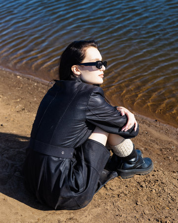 young brunette woman sitting on a sandy beach and getting rest warm autumn weekendの写真素材