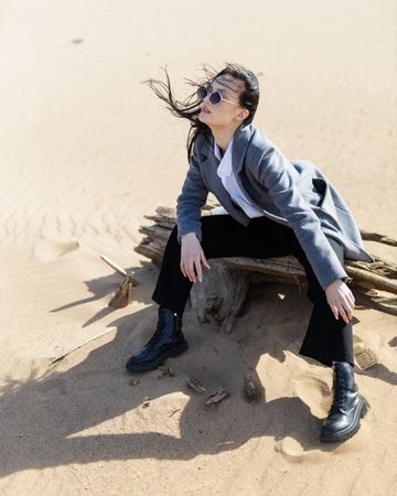 Young woman in warm clothes sitting on river bank alone on cool sunny day, enjoying peace and freedom side view. Outdoor weekend activityの写真素材