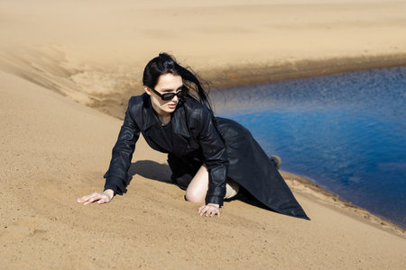 Happy young woman in warm clothes standing fashion posing near river bank alone on cool sunny day, relaxing and enjoying freedom. Outdoors weekend activity, water sceneryの写真素材