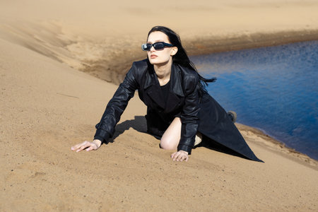 Young woman in warm clothes sitting on river bank alone on cool sunny day, enjoying peace and freedom side view. Outdoor weekend activityの写真素材