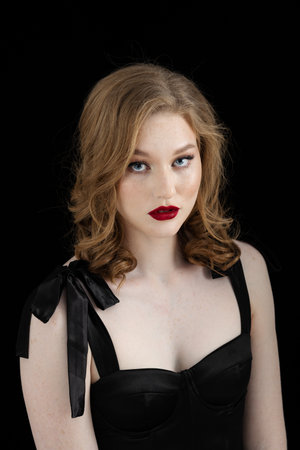 Beauty theme portrait of a beautiful young girl model with freckles on her face in a black dress on a dark background in the studioの写真素材