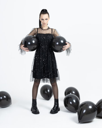Young and beautiful woman look up isolated over white background. Black air balloons in hands. dreamy female in dark dressの写真素材