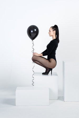 The beautiful long-legged girl with a black balloon poses in studio, she is dressed in black body and black pantyhose, black shoes with a high heel, black brilliant hairの写真素材