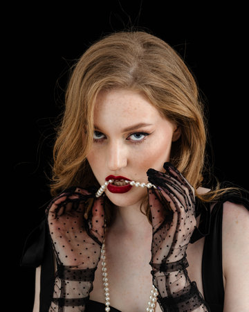 Beauty theme portrait of a beautiful young girl model with freckles on her face in a black dress on a dark background in the studioの写真素材