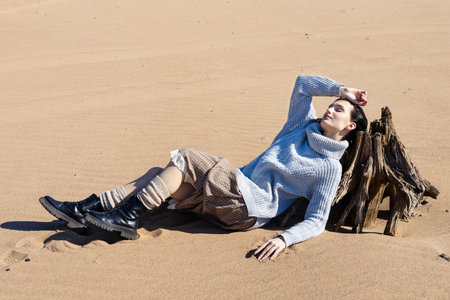 Young woman in warm clothes sitting on river bank alone on cool sunny day, enjoying peace and freedom side view. Outdoor weekend activityの写真素材