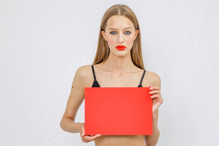 beautiful girl in lingerie with bright red lipstick holds a red billboard in her handsの写真素材