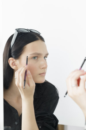 a young girl applies makeup herself at home in front of a mirror