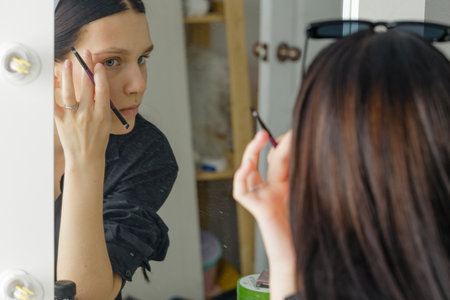 a young girl applies makeup herself at home in front of a mirrorの写真素材