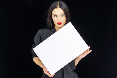 girl shows an empty banner for an inscription on a dark background, a bright brunette in a dark dressの写真素材