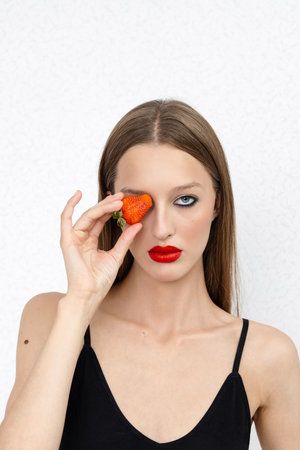 A creative portrait of a beautiful female face holding a red ripe strawberryの写真素材