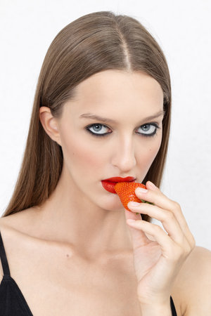 Luscious red lips. Portrait of a beautiful young woman biting into a strawberry.の写真素材