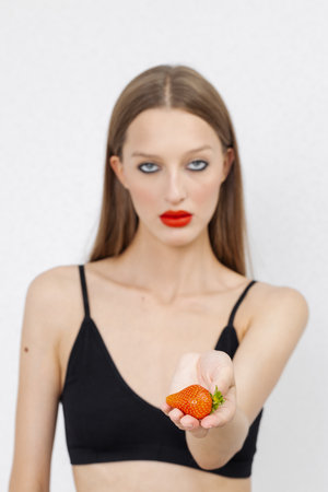 A creative portrait of a beautiful female face holding a red ripe strawberryの写真素材