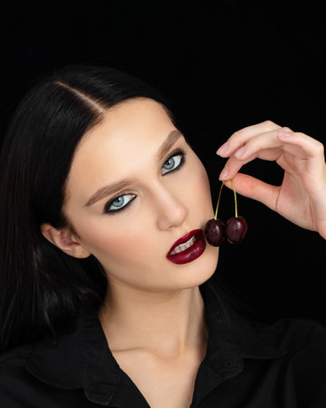 young woman mouth with cherry against black backgroundの写真素材