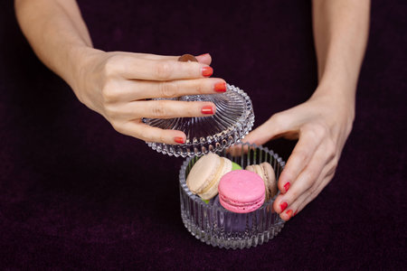 Girl's hand with bright pink manicure hold bright pink halves of macarons on dark background. Closeup view. Making dessert.の写真素材