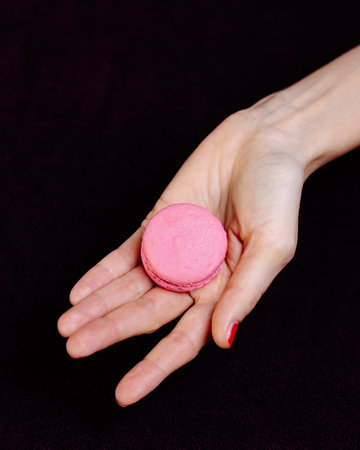 Female hands holding macarons on dark background. Minimalist sweet concept. Top viewの写真素材