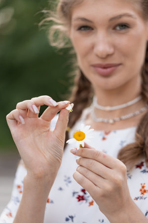 Young lovely smiling woman wonders on flower, tearing petals, close-up.の写真素材