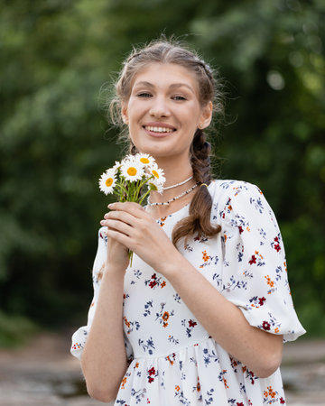 young girl on a hot summer day in a light dress with daisies in her handsの写真素材