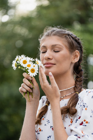 young girl on a hot summer day in a light dress holding a romantic mood with a chamomile flower close to her faceの写真素材