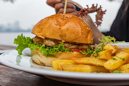 Hamburger with french fries hand with fork in cafeの写真素材