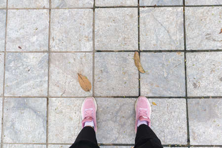 Pink snickers with legs on a grey street with two leafの写真素材