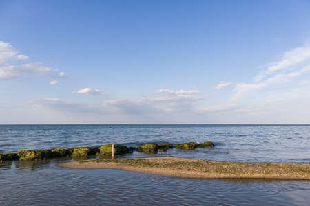 A small sand band leading to a natural breakwater. With blue, clean sky and clouds on background.