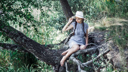 young beautiful girl in straw hat sitting on the shore of the lake. smiling happy girlの写真素材