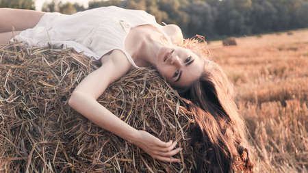 Rural girl on straw bale in a field, Beautiful woman on a haystack