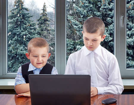Against the background of a window with Christmas trees the boys looking at monitorの写真素材