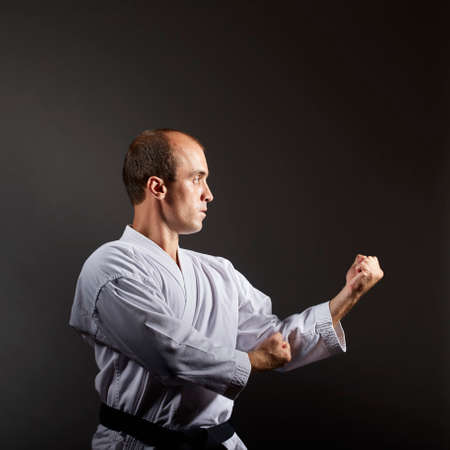 Young athlete trains formal karate exercises on a black background