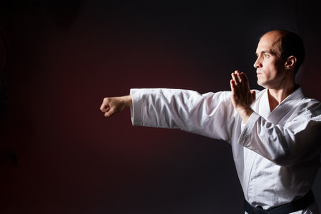 Against a dark red background, a young athlete makes a punch and block with his handの写真素材