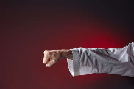 Against a dark red semi-blurred background, a punch in karategiの写真素材