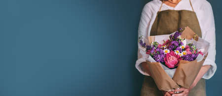 The girl on a blue background holds a bouquet of summer flowers in a paper package. Concept for business, banner and advertising. Copy spaceの写真素材